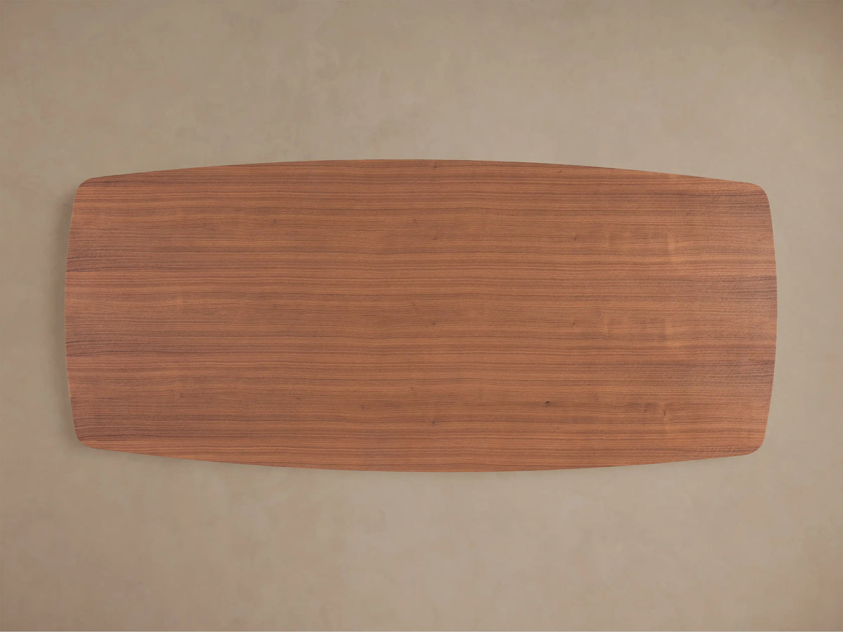 Close-up of Cortina Dining Table, showcasing its smooth American walnut wood surface and elegant, wavy, curved base.
