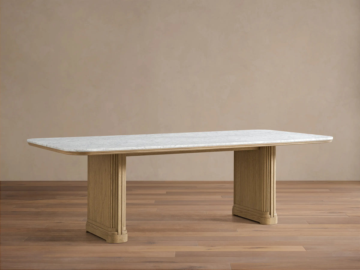 Front view of the Coventry Dining Table, featuring a white Carrara marble top and two light oak reeded pedestal bases.