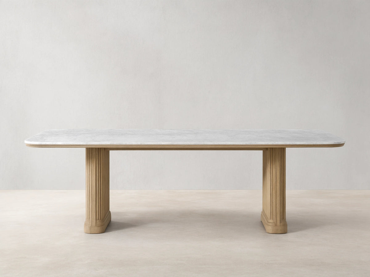 Front view of the Coventry Dining Table with a white Carrara marble top, supported by two oak wood bases with reeded detailing.