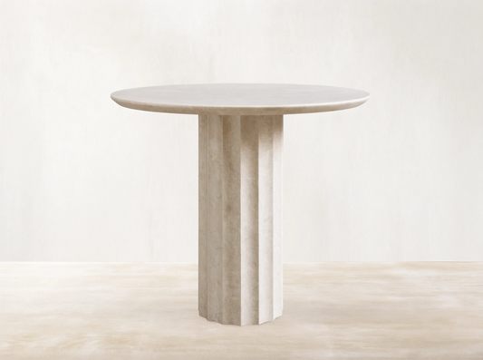 Danae Bistro Table, round light beige marble with a fluted pedestal base, against a neutral wall on a wooden floor.