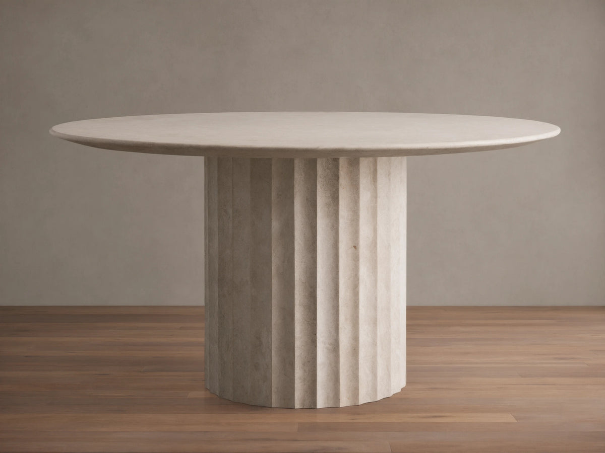 Danae Round Stone Dining Table. Smooth, light beige round marble top on a ribbed cylindrical stone base, on wood floor.