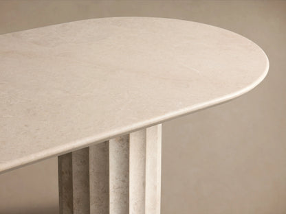 Danae Stone Dining Table with a smooth marble surface and two fluted column bases, set on a wooden floor against a beige wall.