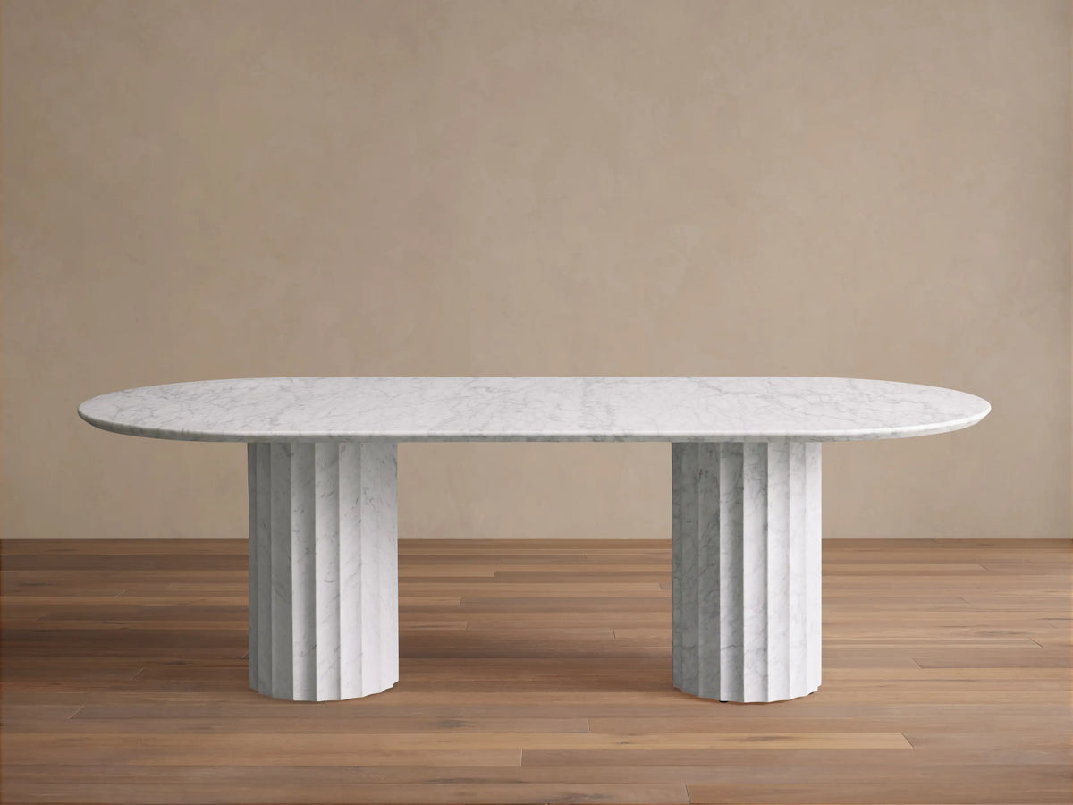 Danae Stone Dining Table: White oval marble top with subtle grey veining, resting on two fluted marble bases on a wood floor.