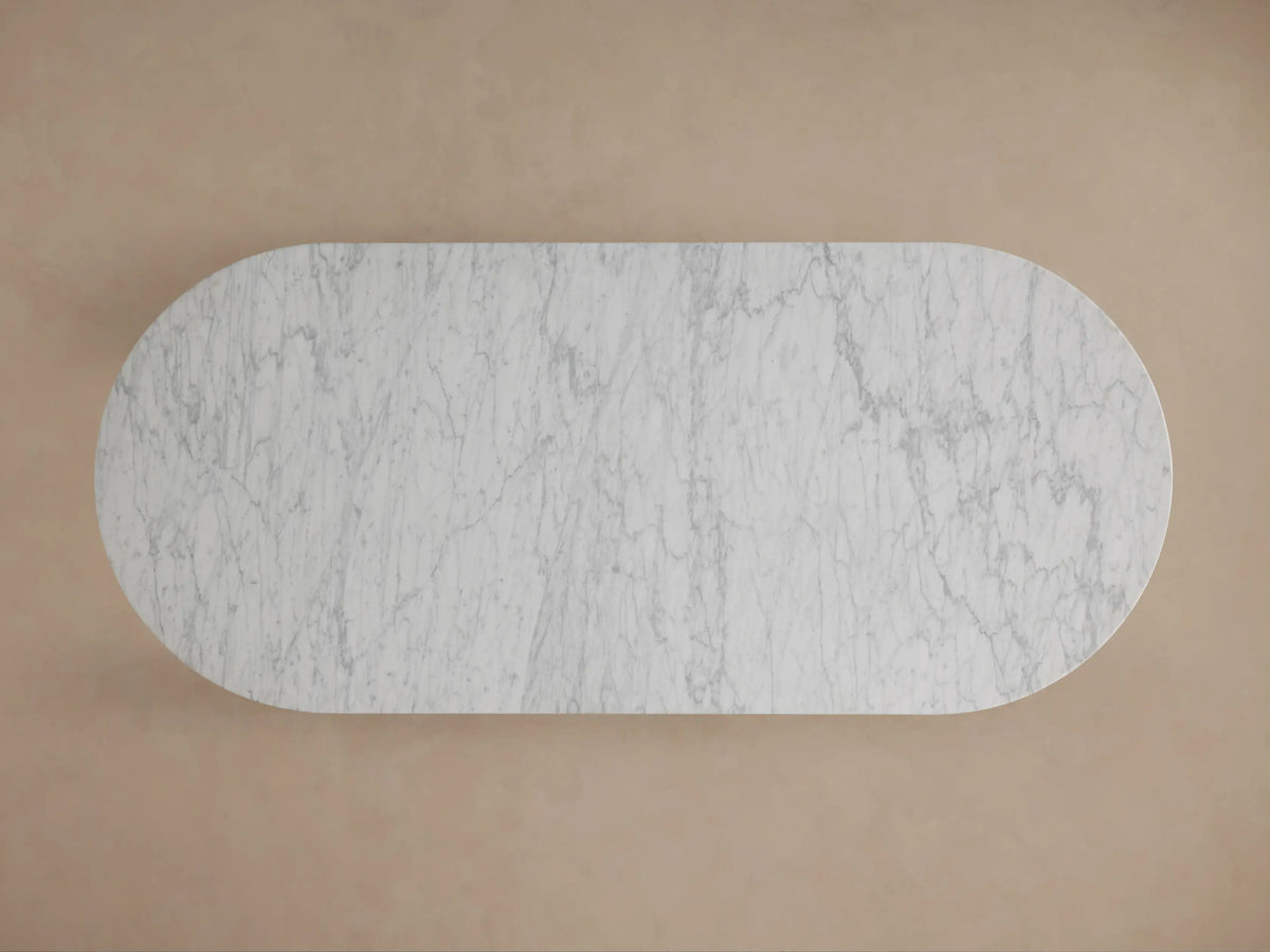 Close-up of Danae Stone Dining Table: white marble top with grey veins, resting on fluted marble columns. Beige background.