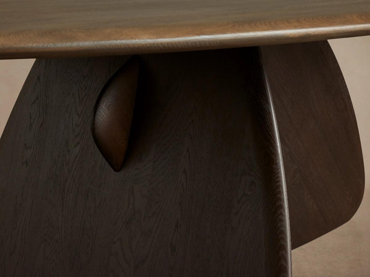 Angled view of Pebble Dining Table with oval russet oak top on a sculptural dark espresso wood base.