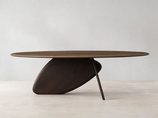 Pebble Dining Table with an oval russet oak top and a dark espresso sculptural, pebble-shaped base with a metal leg.