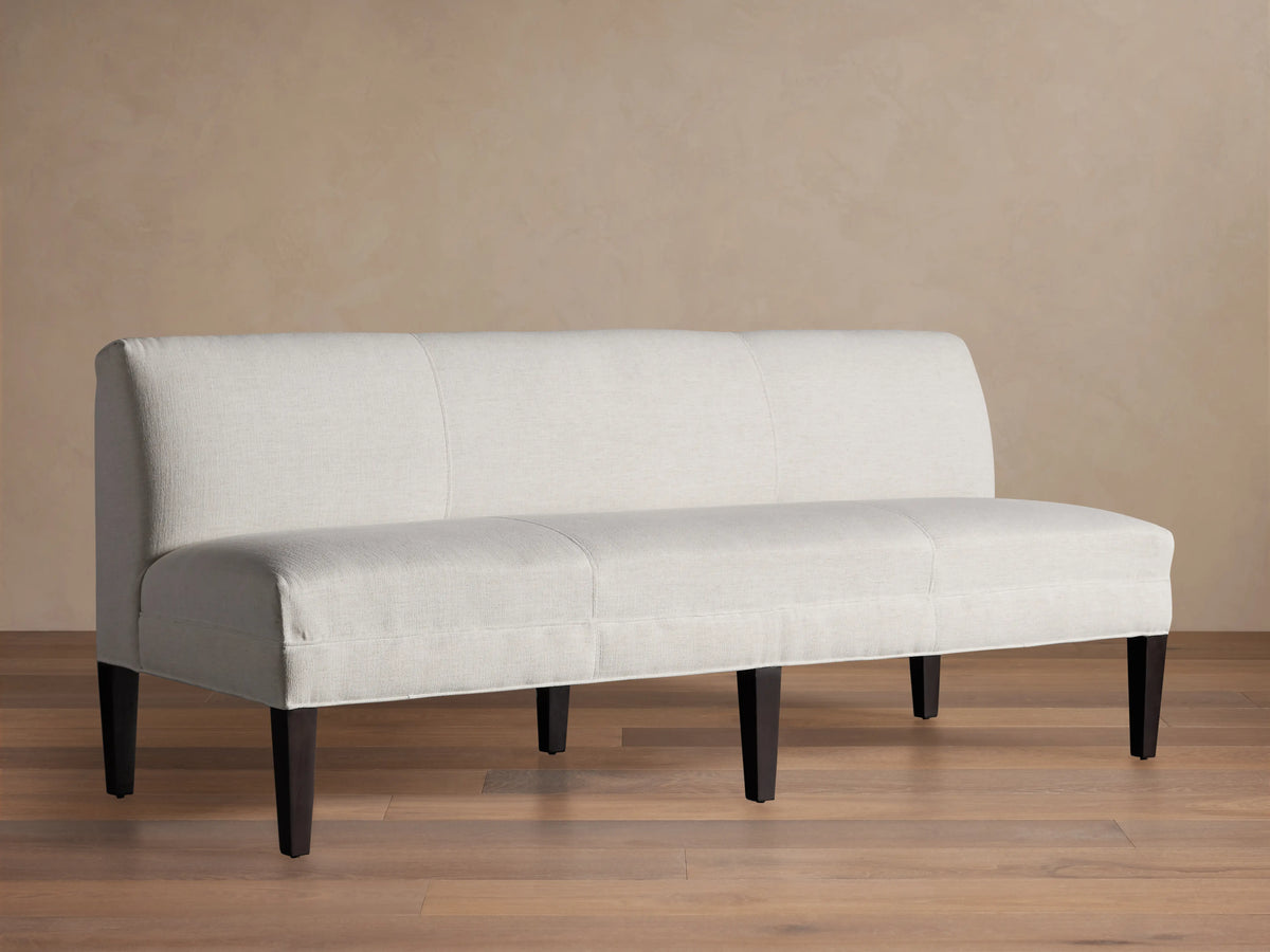 Light-colored Eaton Settee with textured Crypton fabric, channel-stitching, and dark tapered legs, front view against a light wall.