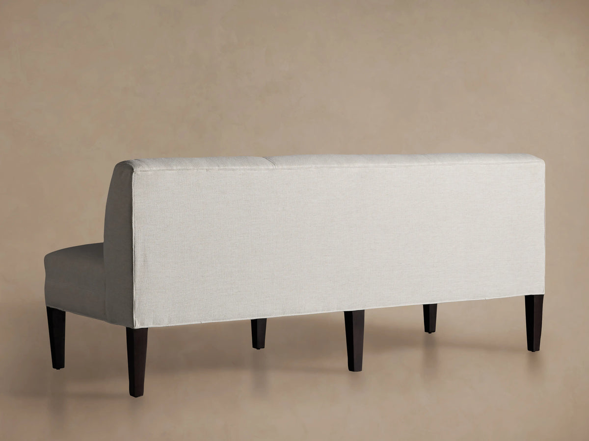 White upholstery on the Eaton Settee with curved backrest and solid maple wood legs. The fabric has subtle channel-stitching detail.