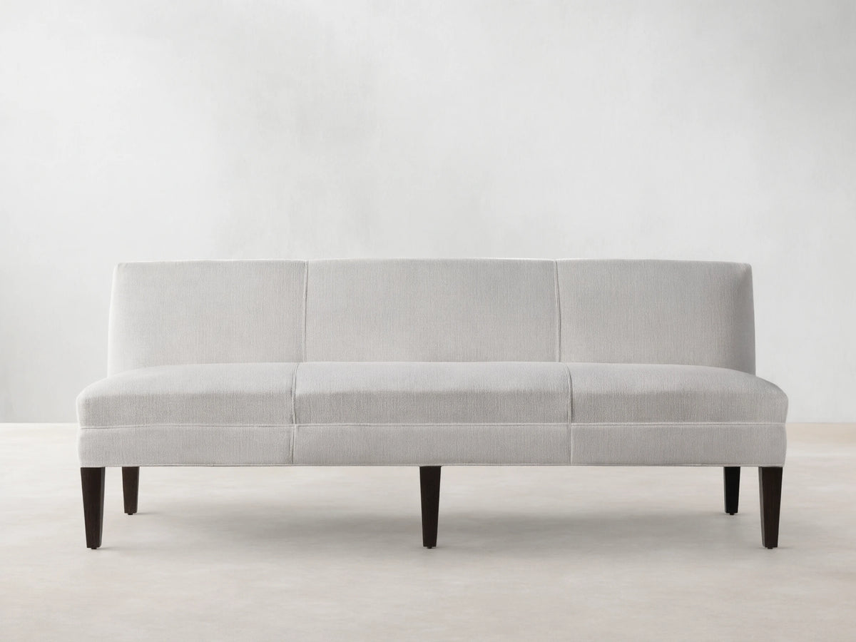 Light-colored Eaton Settee with textured Crypton fabric, channel-stitching, and dark tapered legs, front view against a light wall.