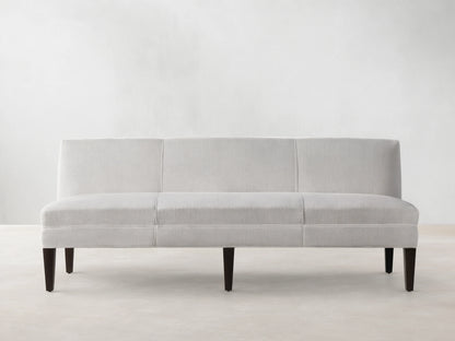 Light-colored Eaton Settee with textured Crypton fabric, channel-stitching, and dark tapered legs, front view against a light wall.