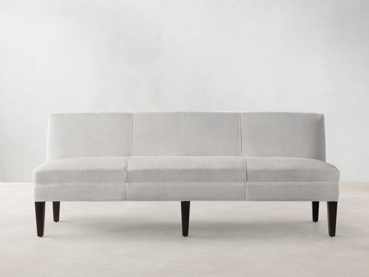 Light-colored Eaton Settee with textured Crypton fabric, channel-stitching, and dark tapered legs, front view against a light wall.