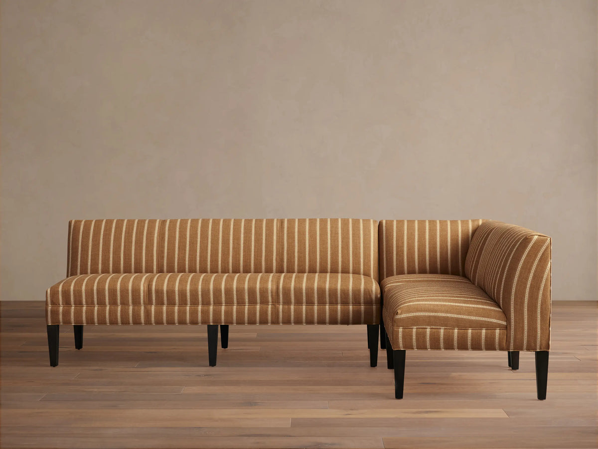 Eaton Banquette, L-shaped, upholstered in brown fabric with vertical white stripes, dark tapered legs, on wood floor.