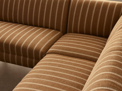 L-shaped Eaton Banquette in golden-brown striped fabric with dark tapered legs, on a light wood floor against a plain wall.