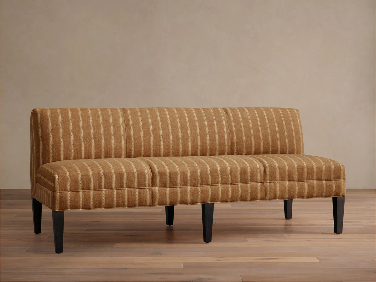 Eaton Settee, golden-brown upholstered with vertical light stripes, dark tapered legs, shown frontally against a light wall.