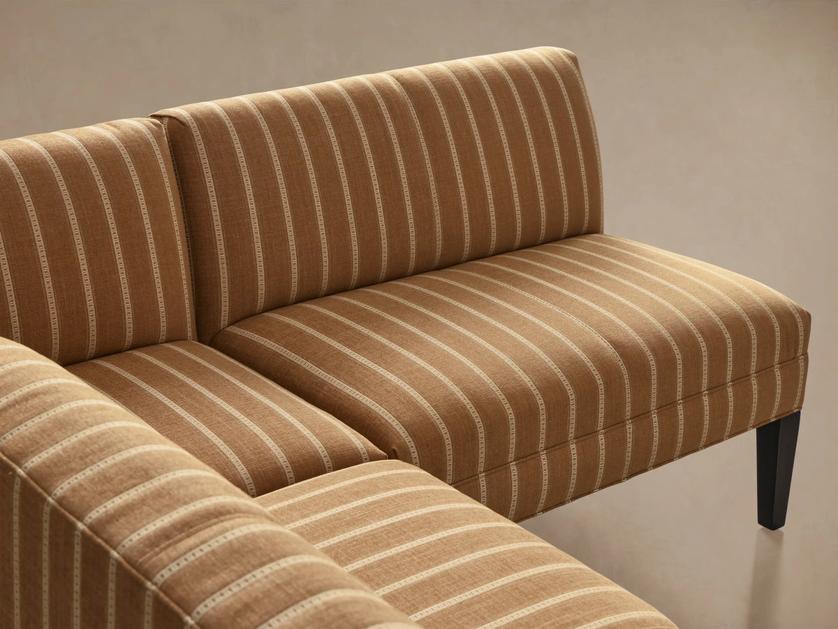 Eaton U-shaped banquette, golden brown with cream vertical stripes, dark tapered legs, shown on a wood floor.