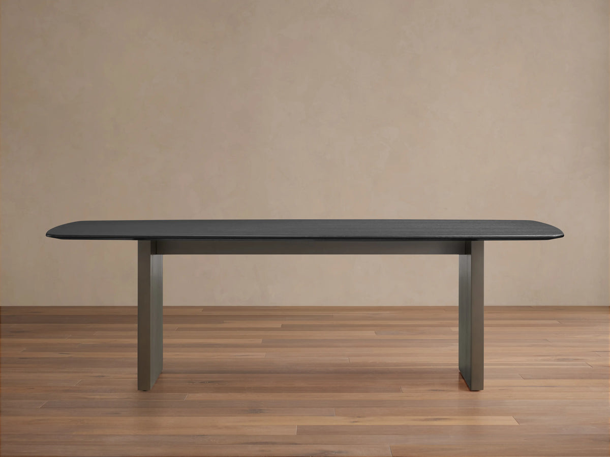 Saint Germain Wood Dining Table with an ebony-finished oak top and steel base, set on a wood floor, against a beige wall.