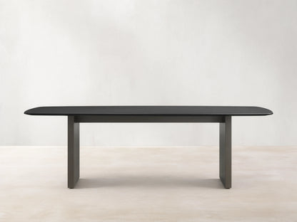 Saint Germain Wood Dining Table with an ebony-finished oak top and steel base, set on a wood floor, against a beige wall.