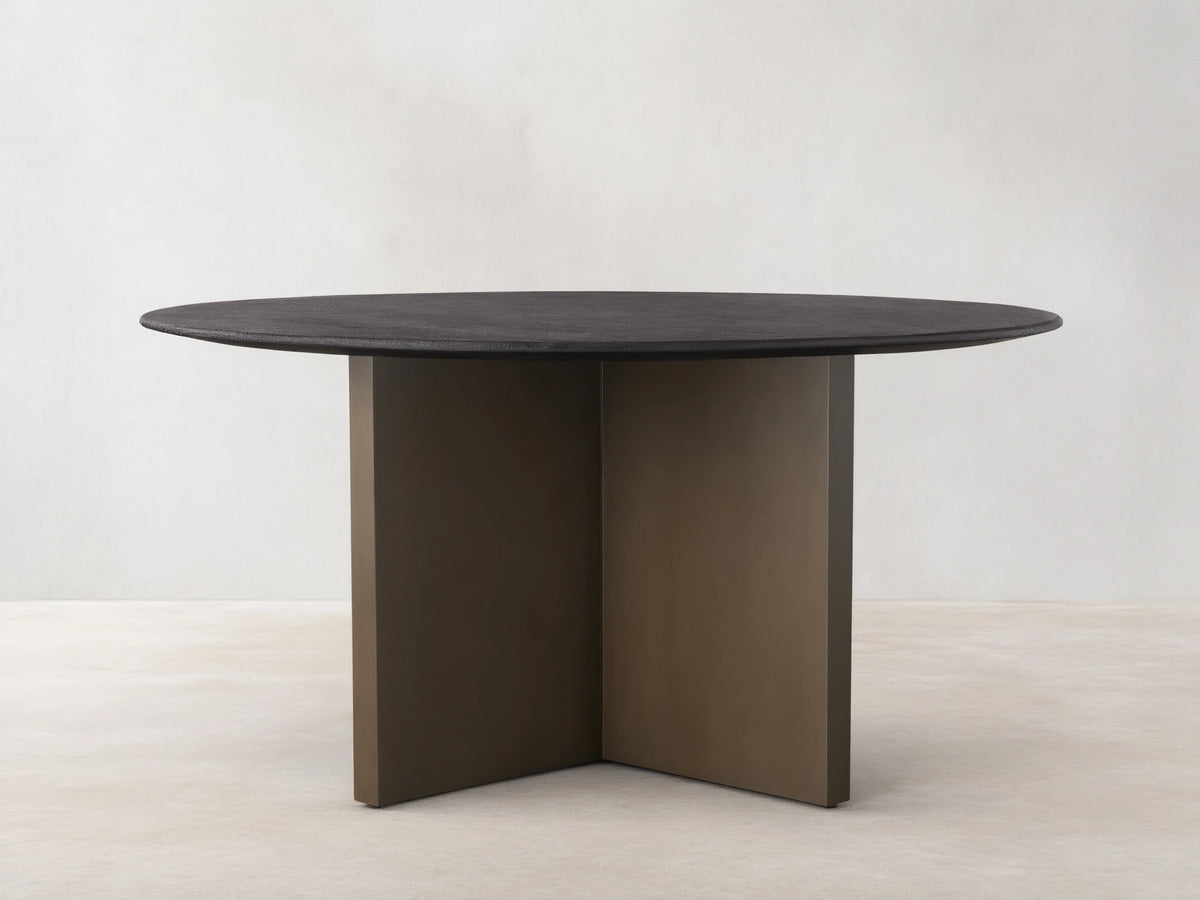 Round Saint Germain dining table with a dark oak tabletop and V-shaped Clement base in a bronze finish, on a wooden floor.
