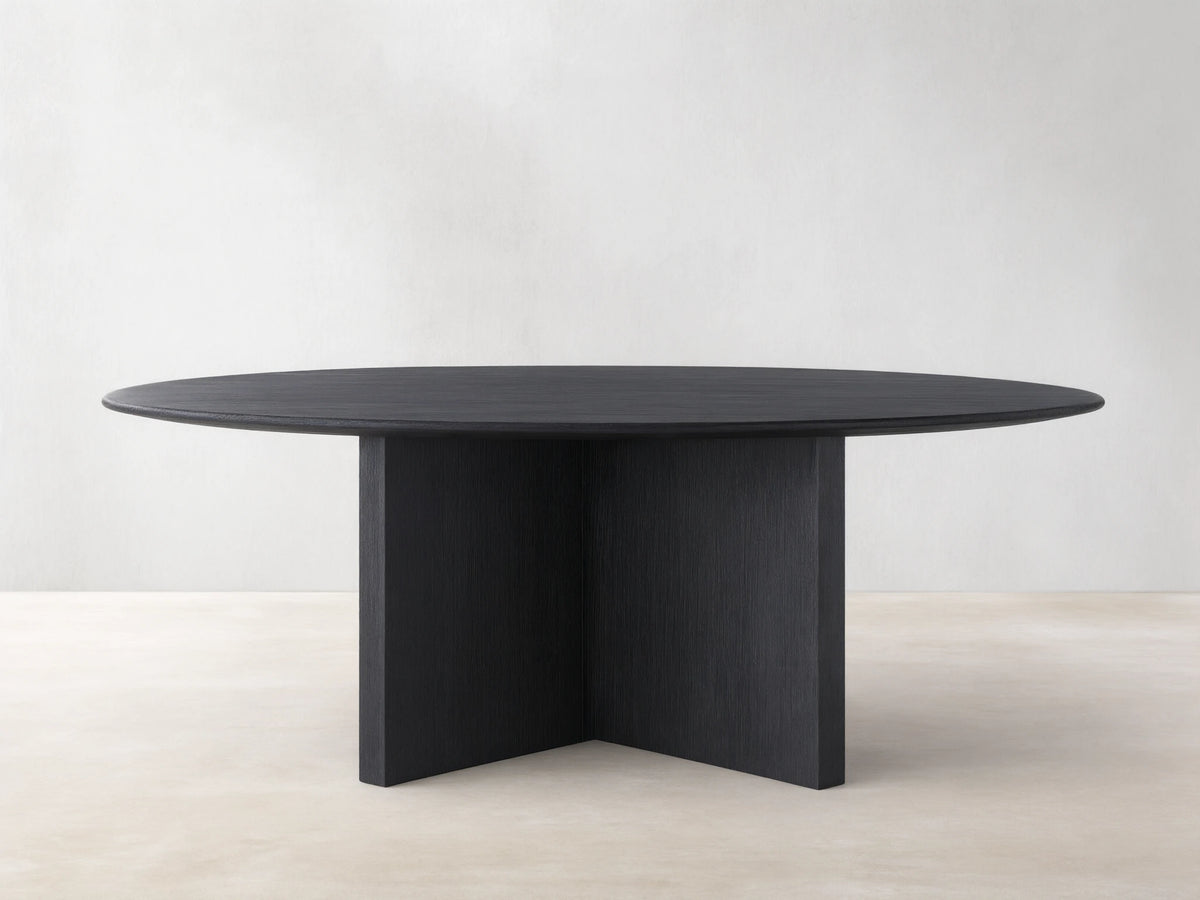 Saint Germain round dining table with an ebony wood top and a sturdy wood base, set on a light wood floor.
