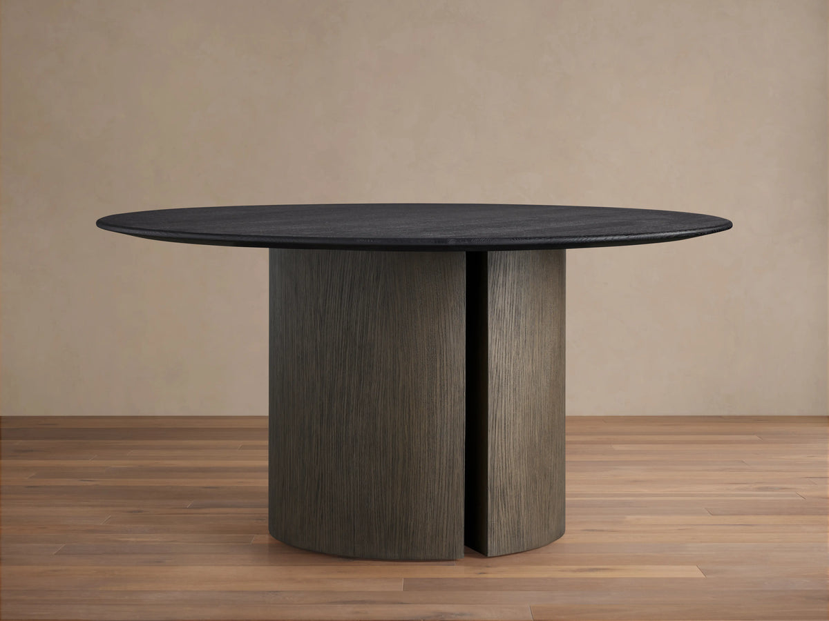 Saint Germain round dining table with a dark solid oak top, set on a sturdy, cylindrical Dauphine base, on a wood floor.
