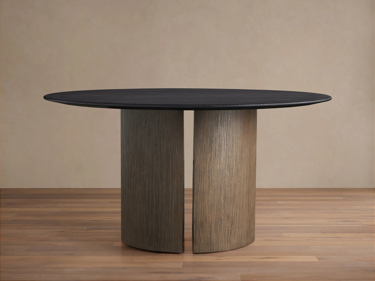 Saint Germain round dining table with a dark solid oak top, set on a sturdy, cylindrical Dauphine base, on a wood floor.