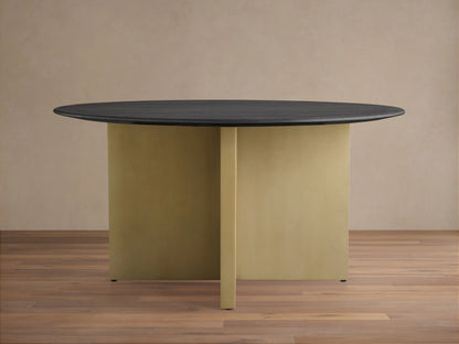 Round wood dining table with a dark ebony tabletop and a V-shaped antique brass base, set on wooden flooring.