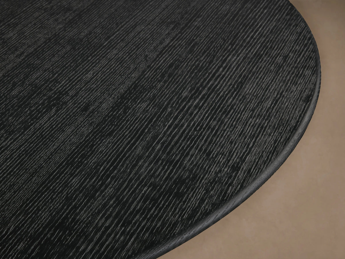 Round dining table with black wood top and golden steel base, in a modern design. Set on wooden floor, neutral wall background.