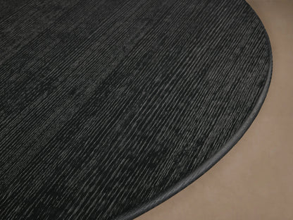 Round dining table with black wood top and golden steel base, in a modern design. Set on wooden floor, neutral wall background.