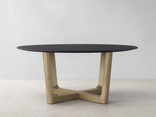 The Saint Germain Round Wood Dining Table features a dark oak tabletop and a wide, V-shaped Rennes base in antique brass on a wood floor.