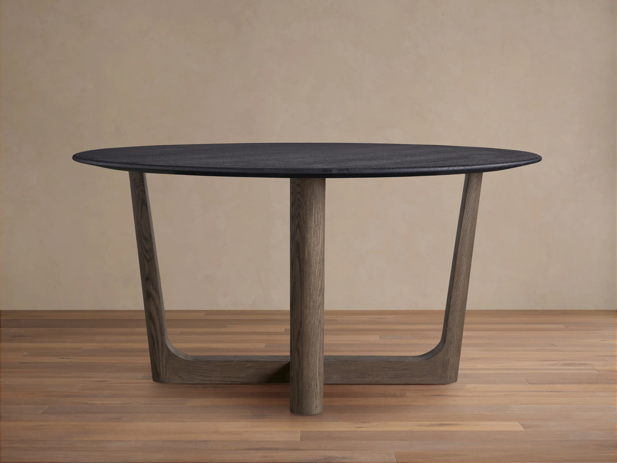Saint Germain round wood dining table with a dark oak tabletop and a geometric Rennes base in a light wood finish, on wooden floor.