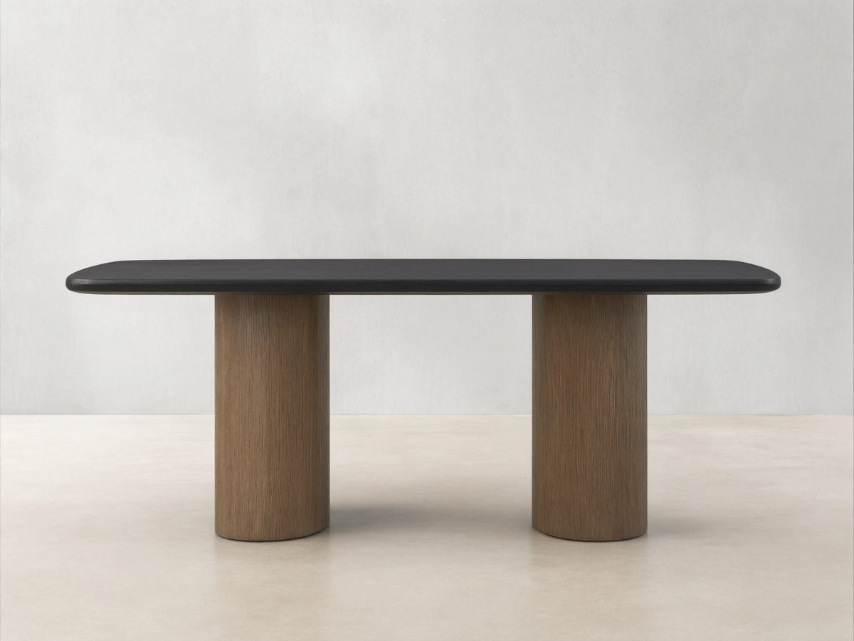 Saint Germain Wood Dining Table with a dark ebony tabletop and two columnar bases in oak, set on a wooden floor.