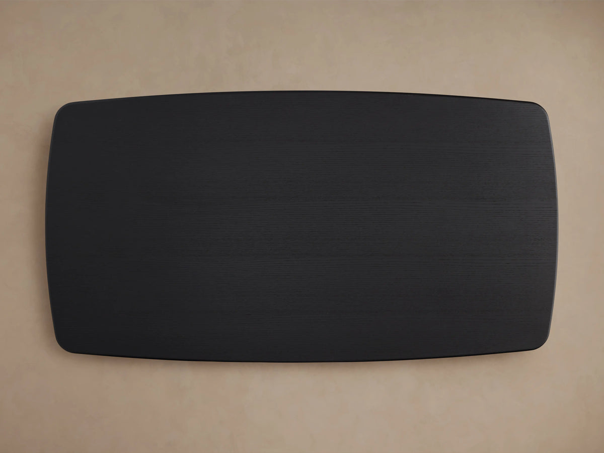 Saint Germain Wood Dining Table with Ebony finish, showing a smooth, dark oak tabletop with visible wood grain, rounded corner, light background.