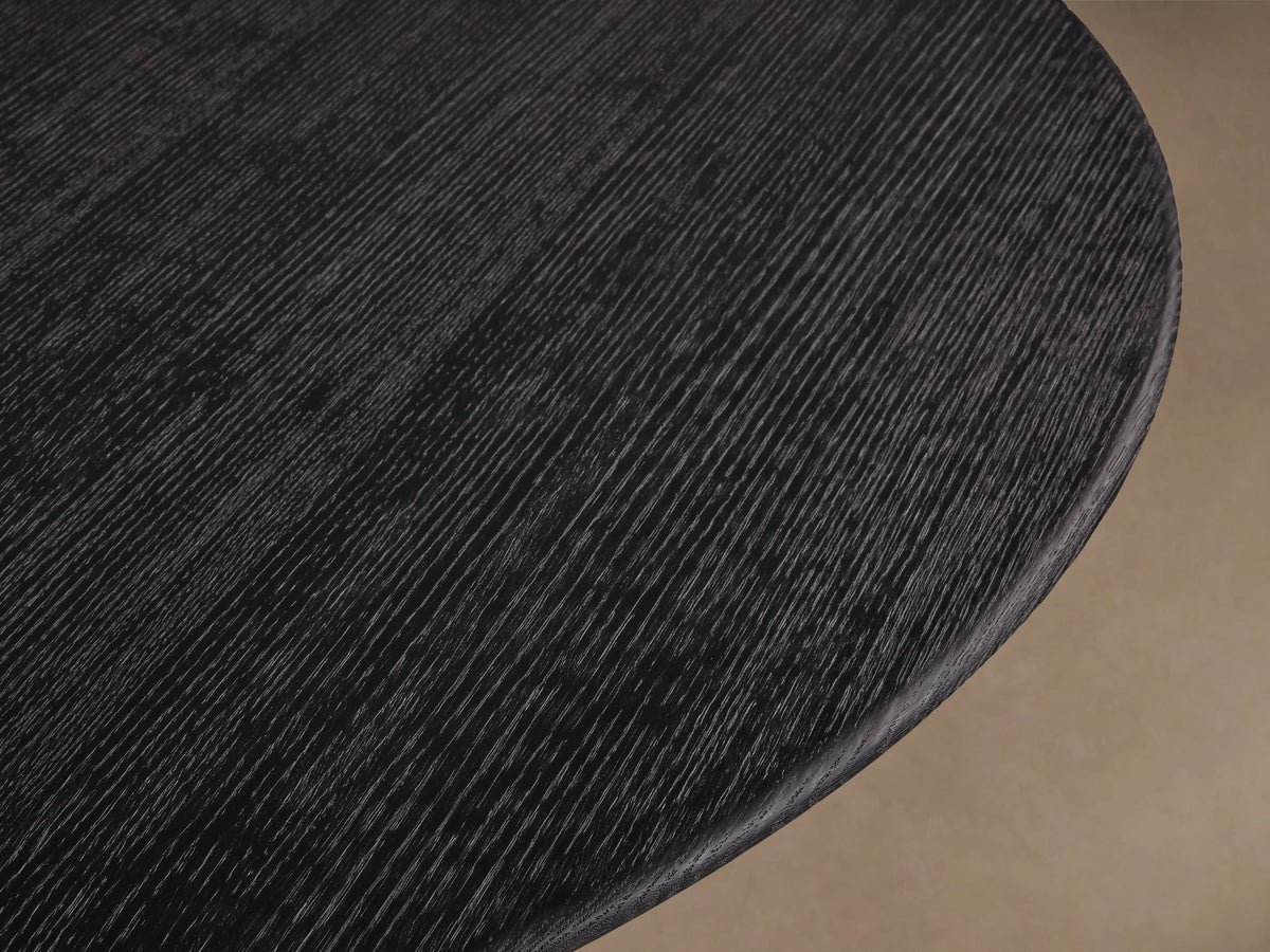 Saint Germain dining table with round dark wood top and dual-toned wood base, set on a wood floor against a neutral wall.