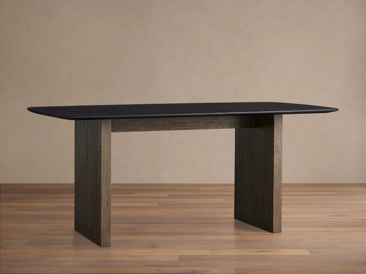 Saint Germain dining table with rectangular black wood top and two thick vertical wood legs, set on light wood flooring.