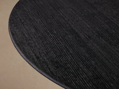 Round dining table with dark wood finish. Flat top supported by a conical base on wood floor against beige wall.