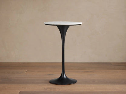 Enzo Bar Table with a round, polished white marble tabletop on a sleek, black tulip-style iron base, set against a wooden floor.