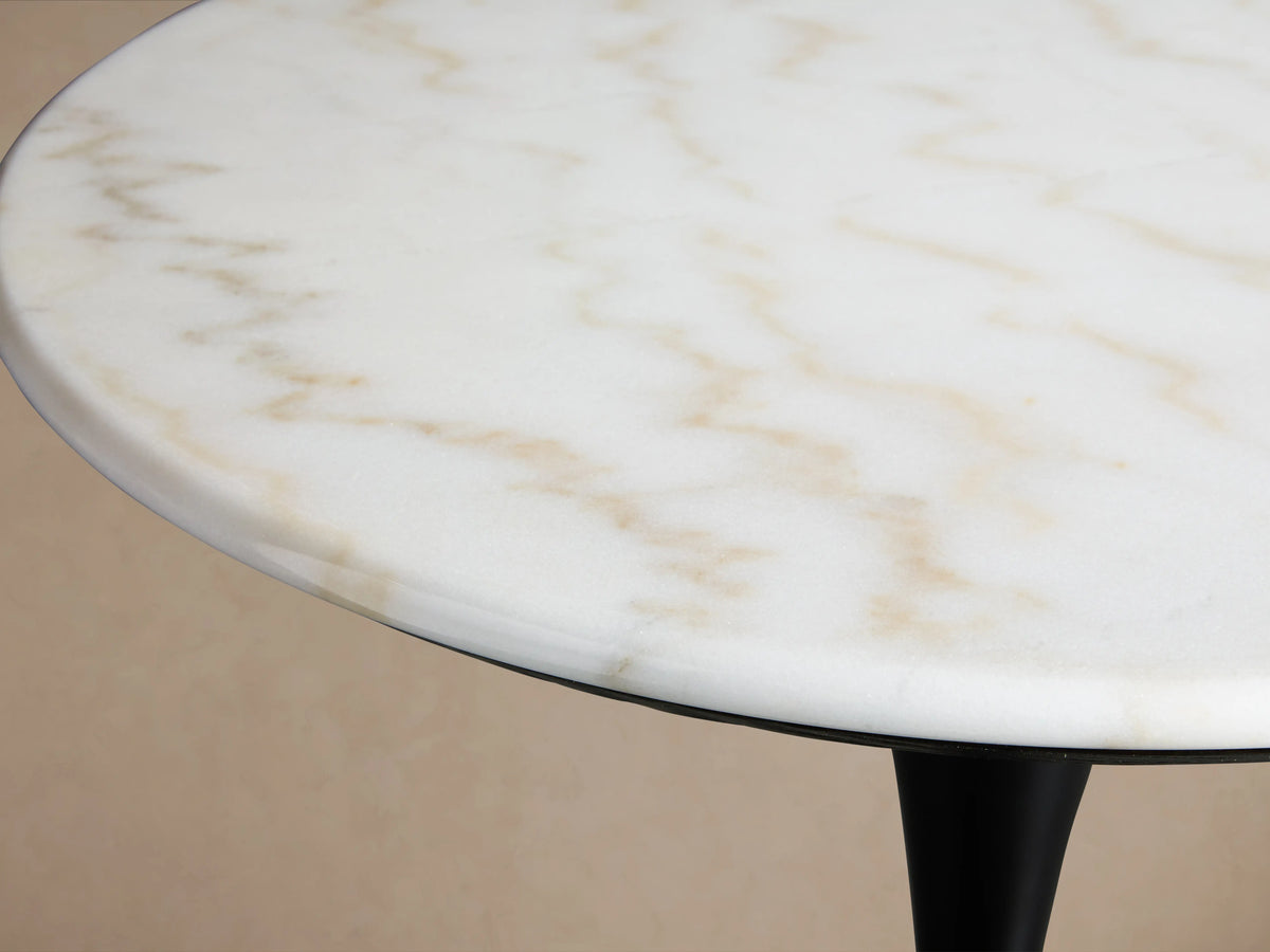 Enzo Bar Table with a round, polished white marble tabletop on a sleek, black tulip-style iron base, set against a wooden floor.
