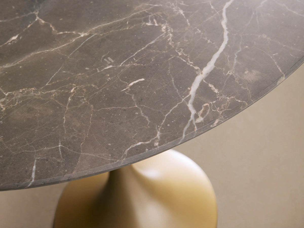 Saint Germain Counter Table with round Carrara marble top, supported by a sleek, metallic gold steel base on wooden floor.