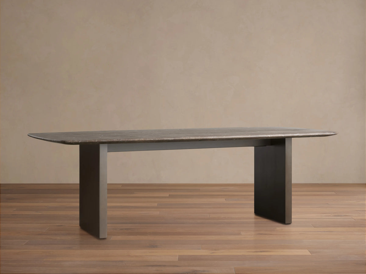 Saint Germain Stone Dining Table with a flat stone tabletop and a Clement Base in dark finish, placed on a wooden floor against a plain wall.