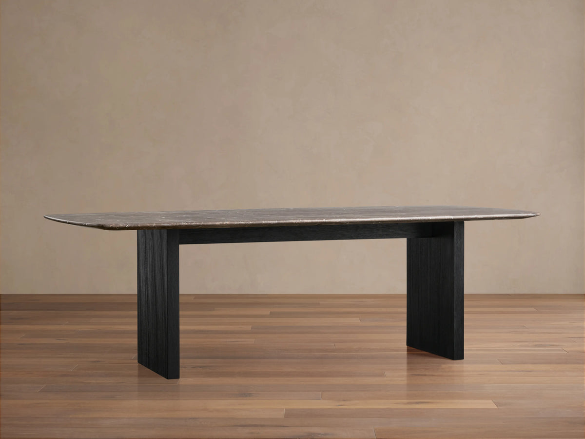 Saint Germain dining table with a dark stone top and a black wooden base on a wooden floor, against a beige wall.
