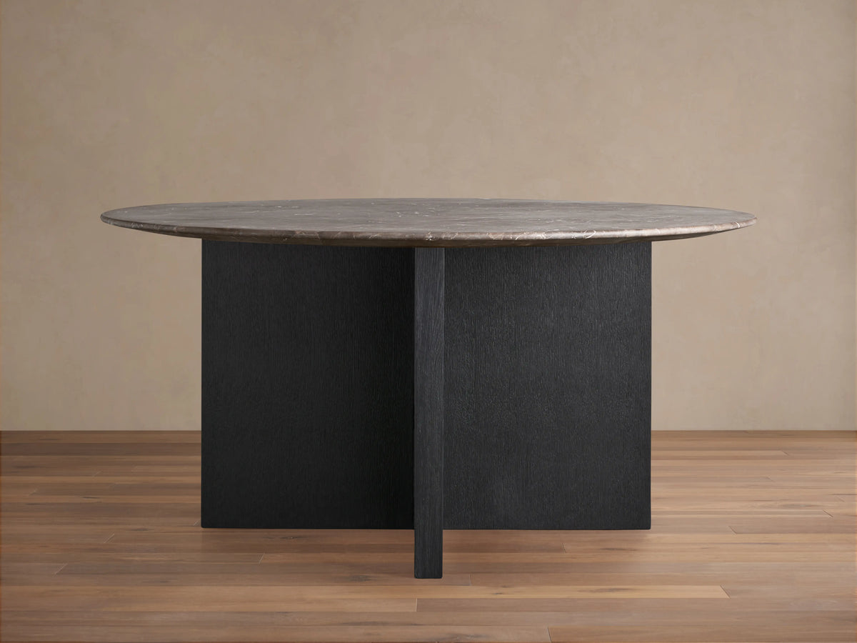 Saint Germain dining table with dark stone top and ebony oak veneer base on wooden floor, against beige backdrop.