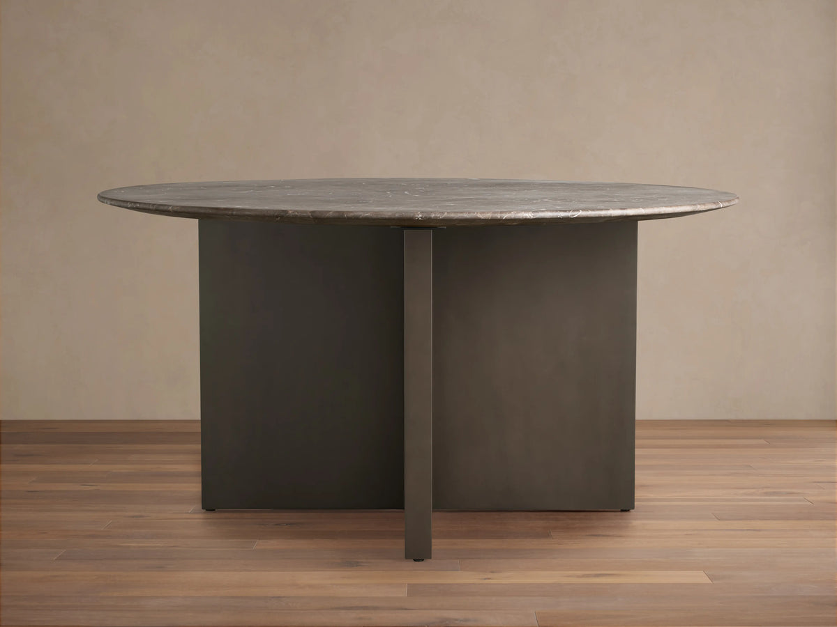 Saint Germain Round Stone Dining Table with a dark stone top and two-tone Clement base on a wooden floor.
