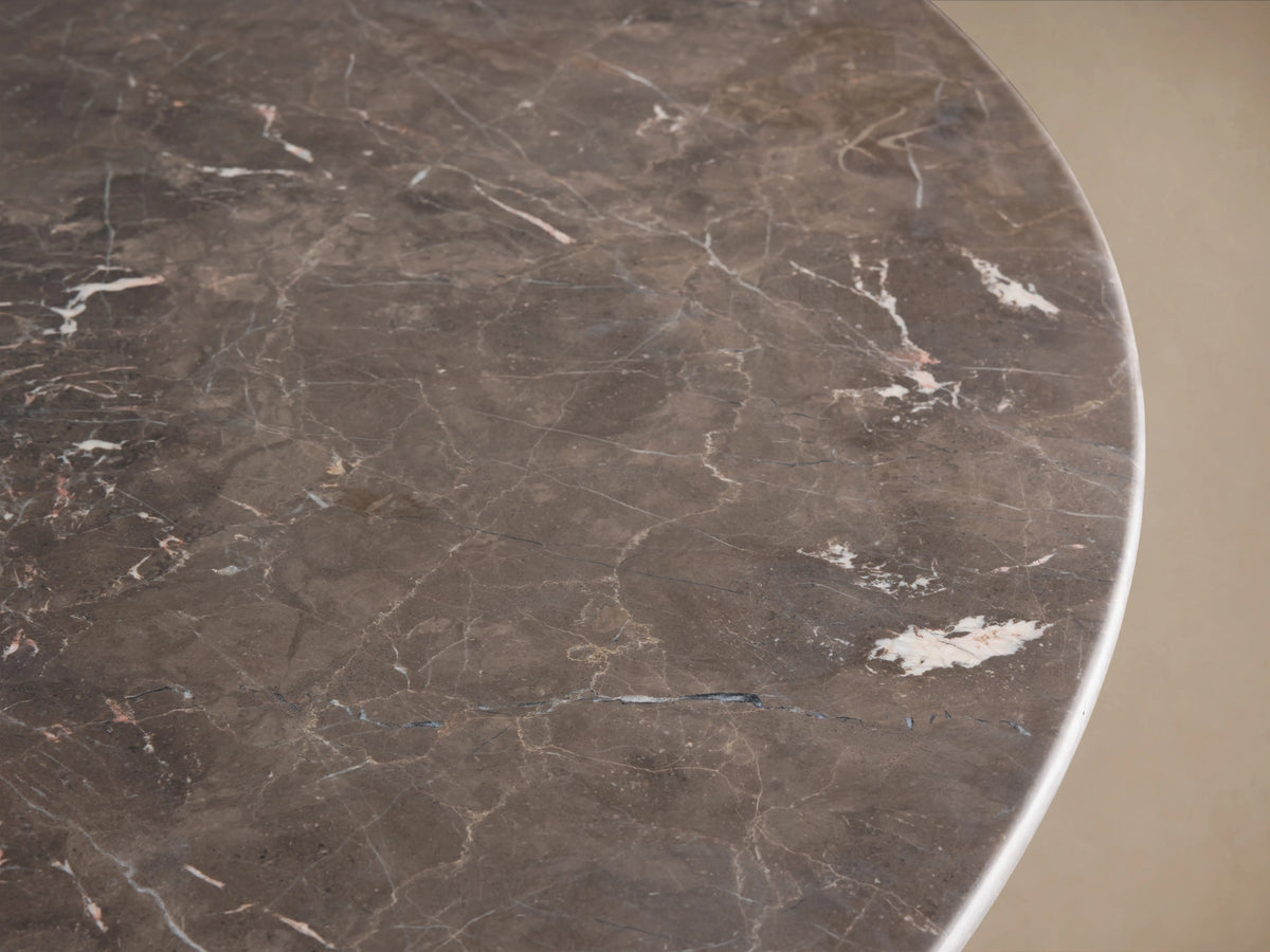 Round dining table with grey stone tabletop, displaying natural variations. Features a dual-panel base finished in a dark brown shade, set on wooden flooring.