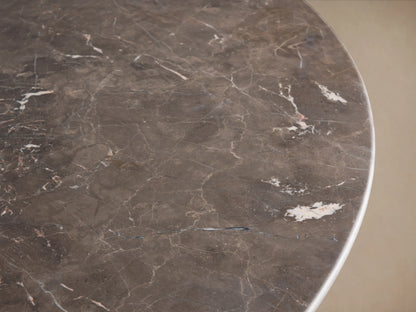Round dining table with grey stone tabletop, displaying natural variations. Features a dual-panel base finished in a dark brown shade, set on wooden flooring.