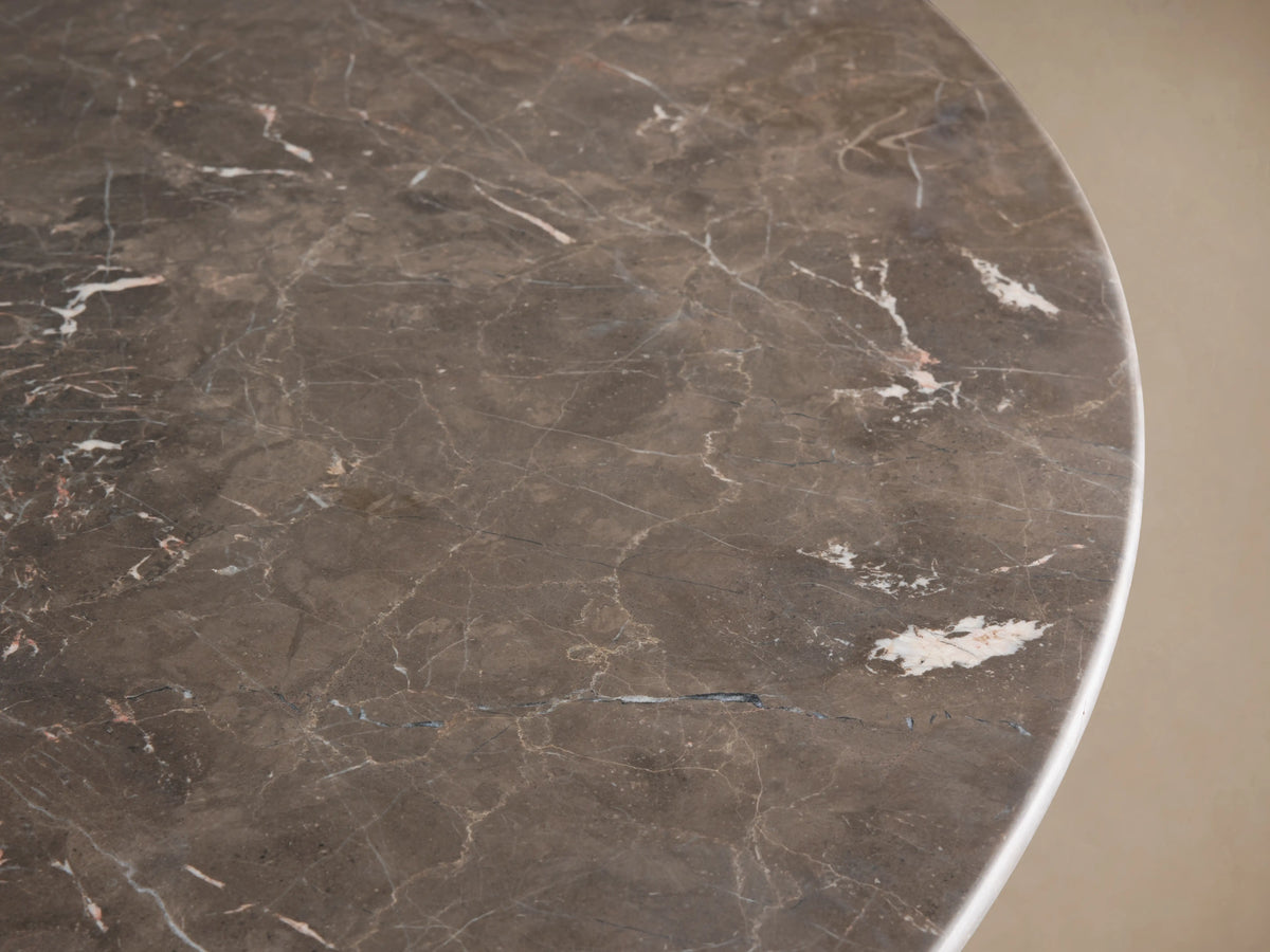 Saint Germain Round Stone Dining Table with a dark marble top and elegant gold steel tulip-shaped base on a wooden floor.