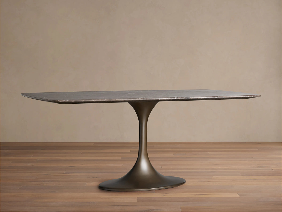 Saint Germain Stone Dining Table with a rectangular marble top and a sleek, bronze-toned Launette steel base, on a wooden floor.