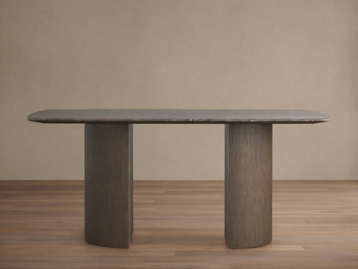Stone Dining Table with oval Carrara marble top, gray-brown color, and dual cylindrical oak veneer bases on wood floor.