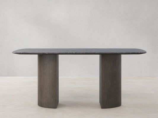 Stone Dining Table with oval Carrara marble top, gray-brown color, and dual cylindrical oak veneer bases on wood floor.