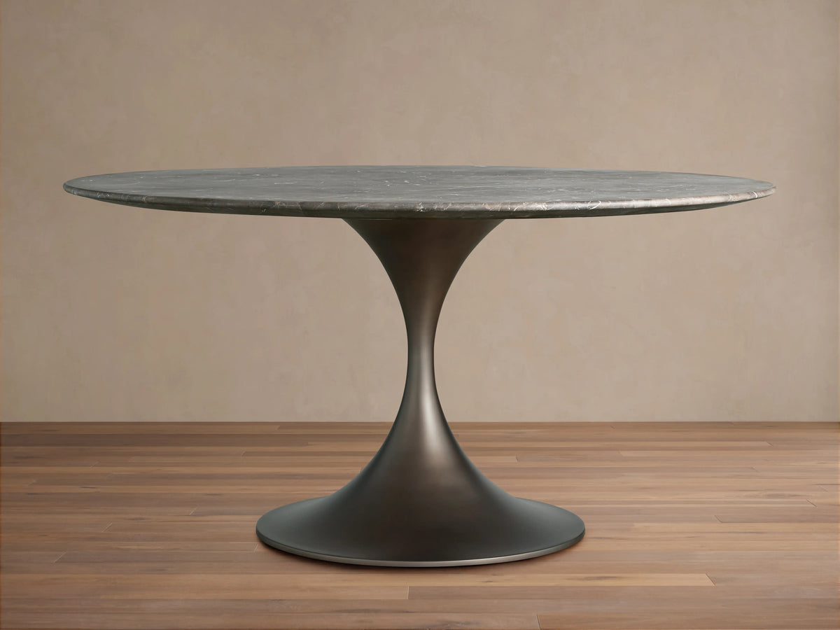Saint Germain Round Dining Table with a dark metal base and a smooth, circular stone tabletop, set on wooden flooring.