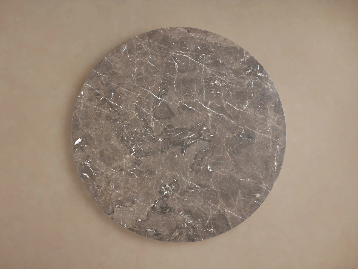 Saint Germain Round Stone Dining Table with marble top and elegant steel Launette base on wooden floor, set against beige wall.